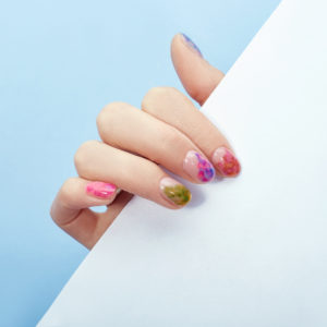 Hand cosmetics nails coloring and care, professional manicure and care product. Hand lying on a colored paper background